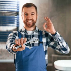 holding-wrenches-plumber-in-blue-uniform-is-at-work-in-the-bathroom-e1676320710493.jpg